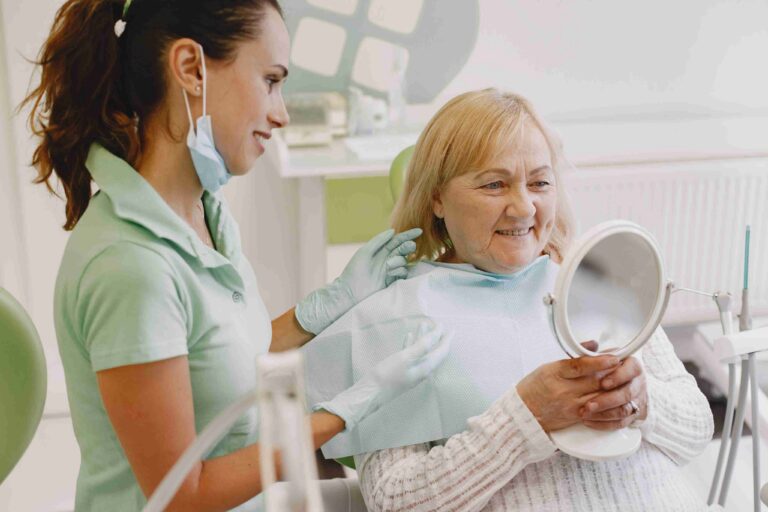 Senior patient smiling with mirror after treatment.